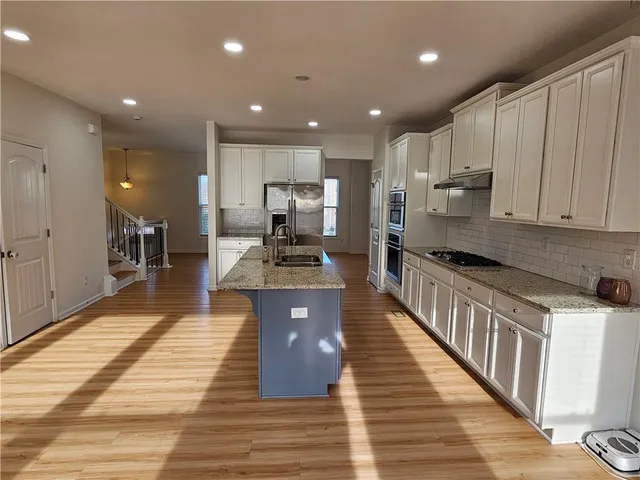 a large kitchen with stainless steel appliances granite countertop a large counter top and a stove top oven with wooden floor