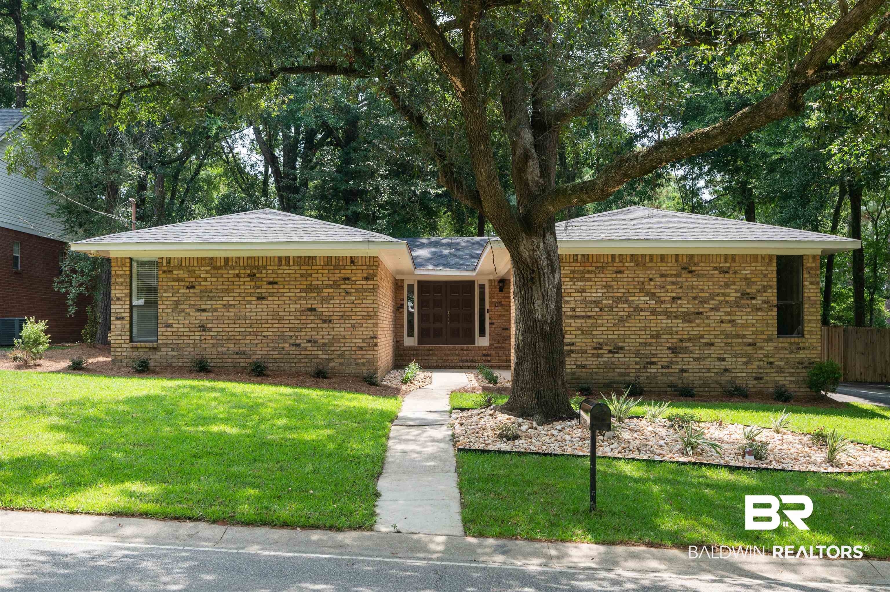 599 Ridgewood Drive Daphne, AL 36526 - Photo 1 of 41 Brick exterior with a prominent mature tree, featuring a symmetrical design, a paved walkway, and manicured landscaping with ground cover plants