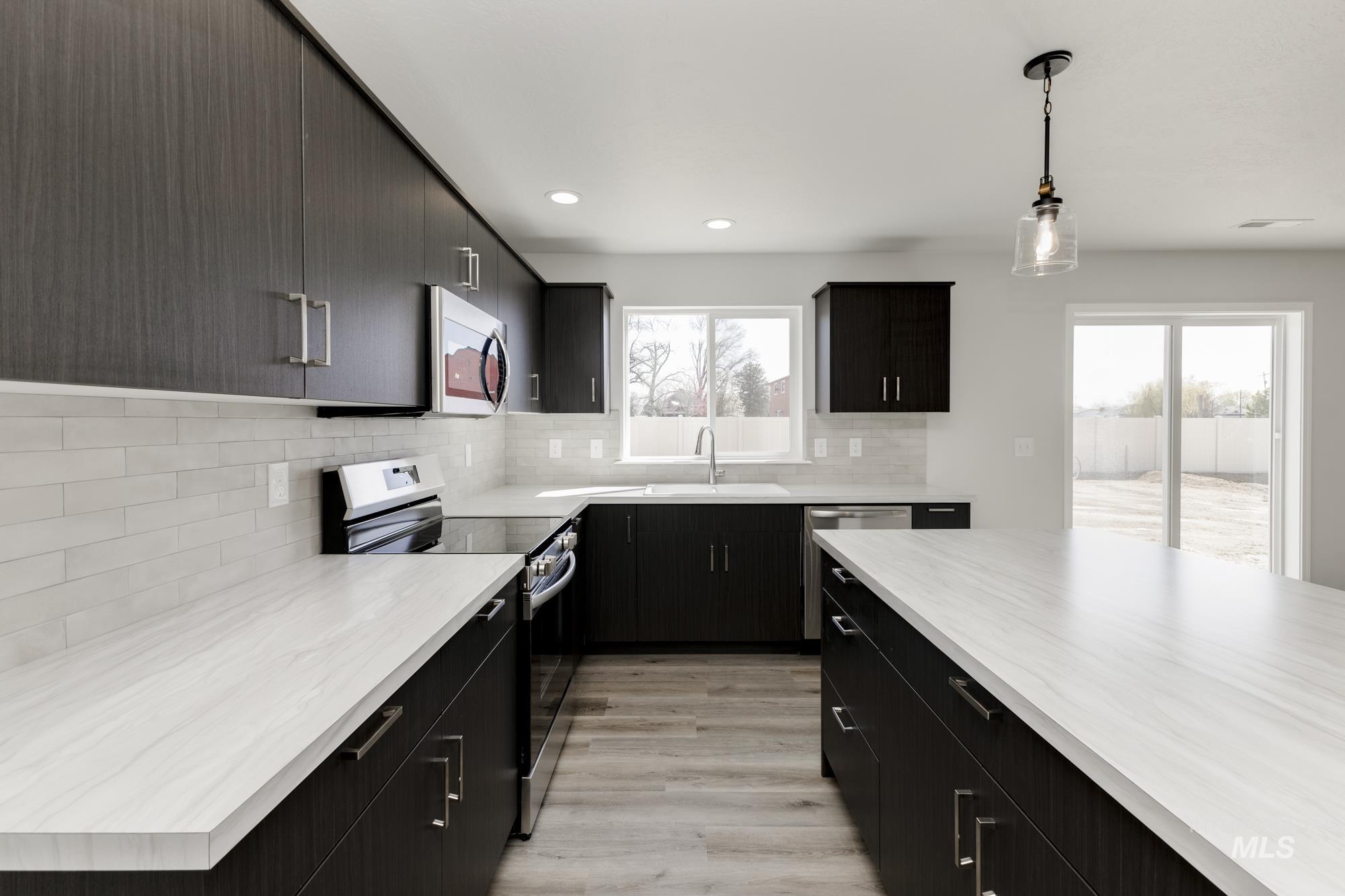 13681 Inman Court Caldwell, ID 83607 - Photo 5 of 31 Kitchen with stainless steel appliances, dark cabinets, hanging light fixtures, light wood-style floors, and modern cabinets