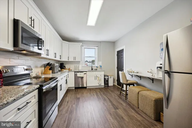 a kitchen with stainless steel appliances granite countertop a refrigerator a stove top oven a sink dishwasher and white cabinets with wooden floor