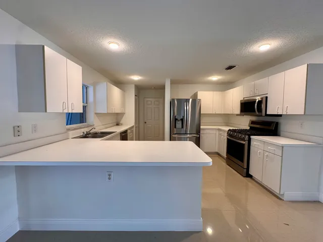 a large kitchen with stainless steel appliances granite countertop a stove a sink a refrigerator and white cabinets with wooden floor