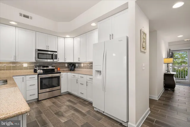 a kitchen with stainless steel appliances kitchen island granite countertop a refrigerator a stove top oven a sink dishwasher and a dining table with wooden floor