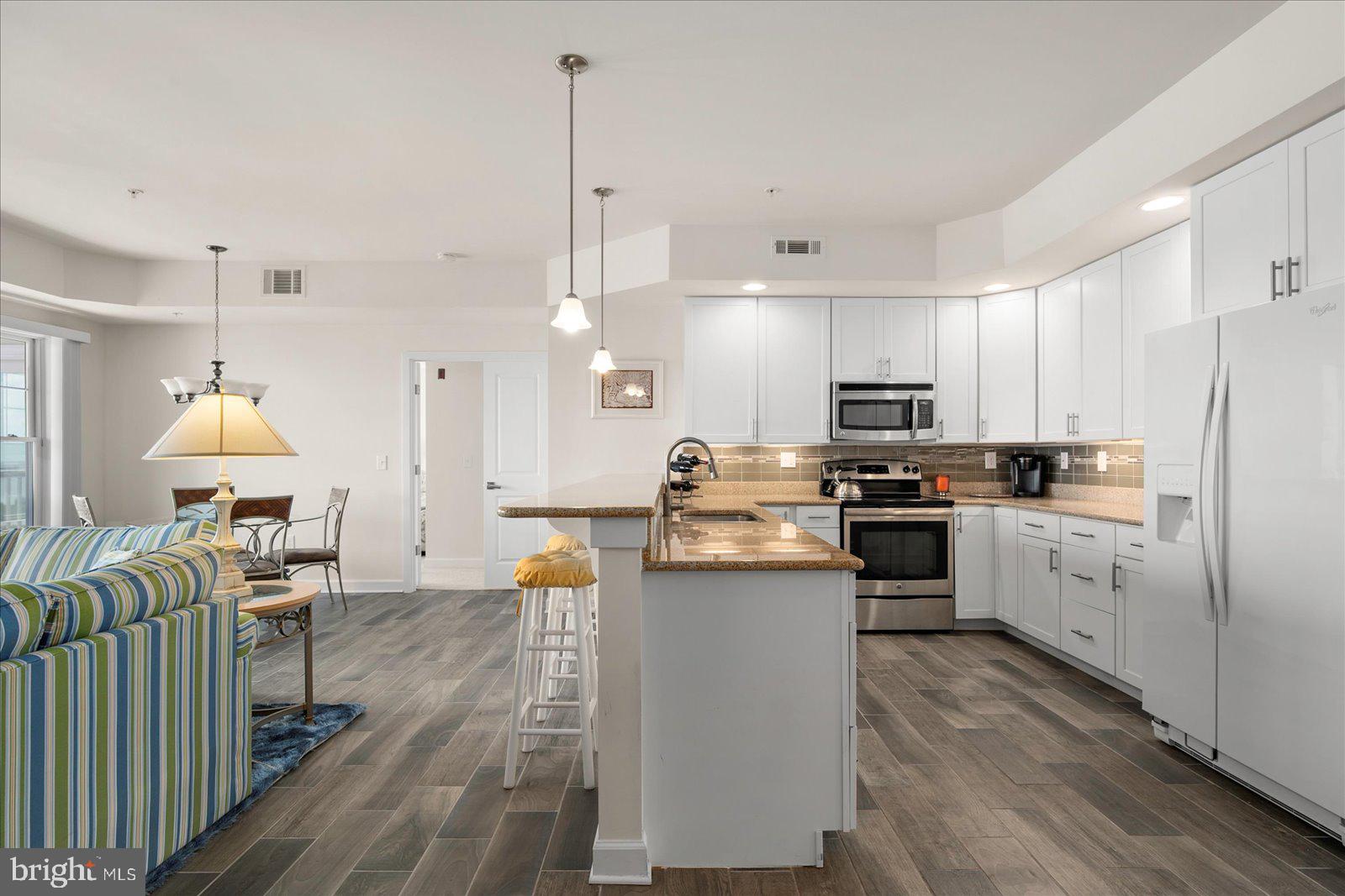 37292 Lighthouse Road, Unit 202 Selbyville, DE 19975 - Photo 21 of 78 a kitchen with stainless steel appliances kitchen island granite countertop a refrigerator a stove top oven a sink dishwasher and a dining table with wooden floor