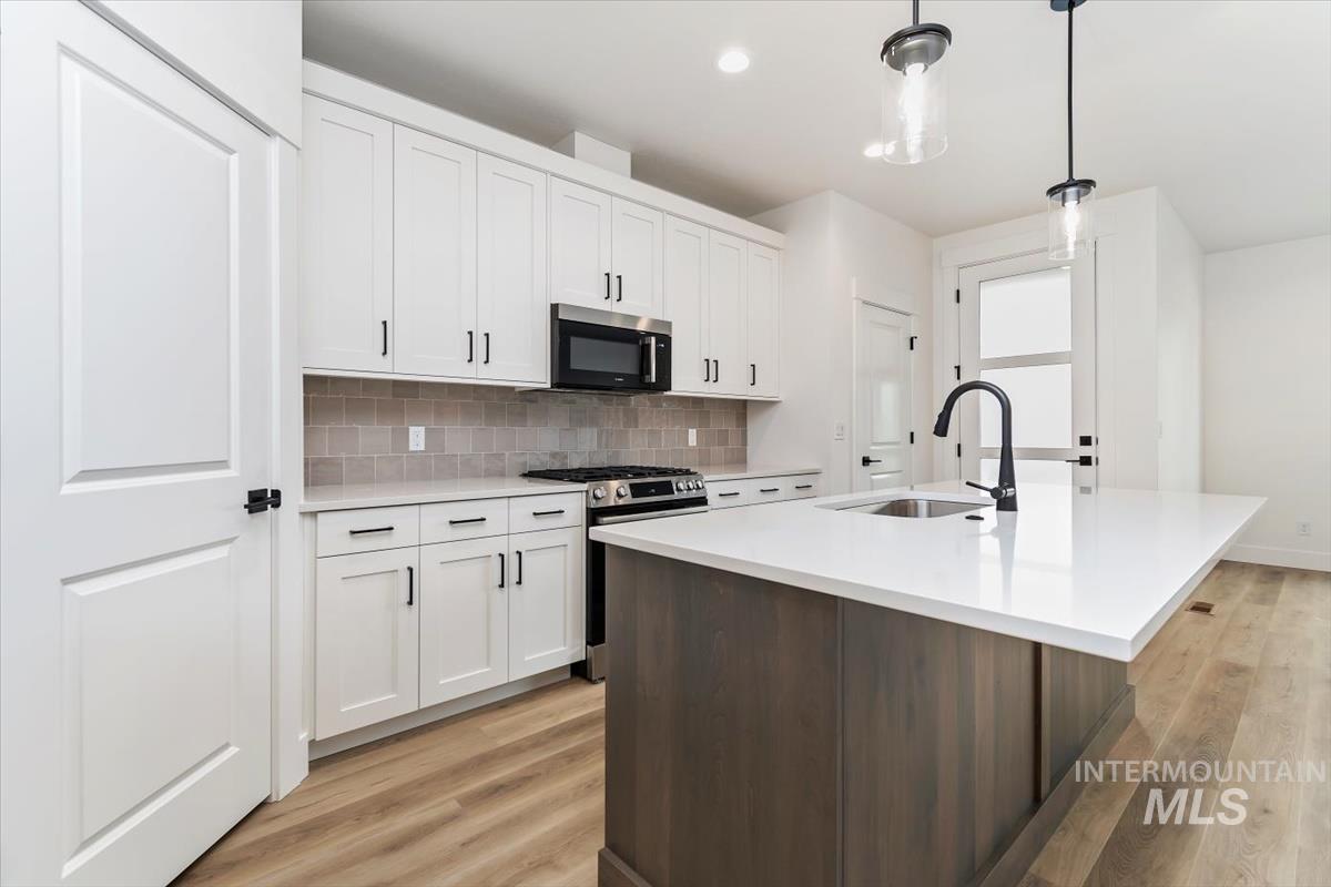 752 South Calhoun Place Star, ID 83669 - Photo 9 of 40 Kitchen featuring light wood finished floors, stainless steel appliances, a center island with sink, dual tone cabinets, and hanging light fixtures
