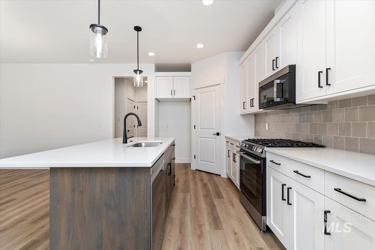 752 South Calhoun Place Star, ID 83669 - Photo 5 of 40 Kitchen featuring stainless steel appliances, two tone cabinets, a center island with sink, hanging light fixtures, and light stone countertops