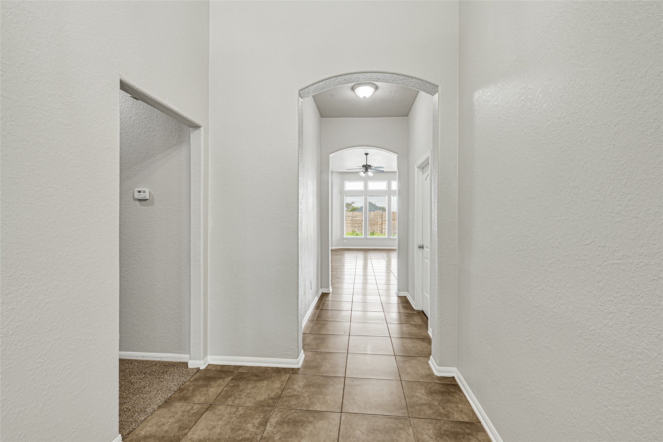 4702 Sedgewood Drive Rosenberg, TX 77471 - Photo 5 of 24 This home showcases a bright hallway with tiled flooring, leading to living room with large windows and a ceiling fan. The space feels open and inviting, with neutral walls and an arched doorway adding architectural interest.