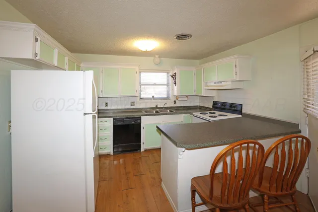 a kitchen with stainless steel appliances granite countertop a refrigerator a sink a stove and white cabinets with wooden floor