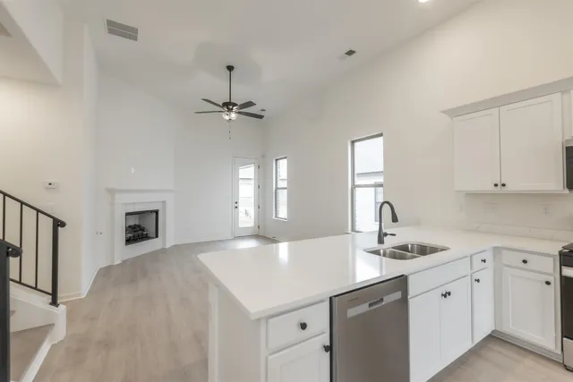 a kitchen with a sink dishwasher and white cabinets with wooden floor