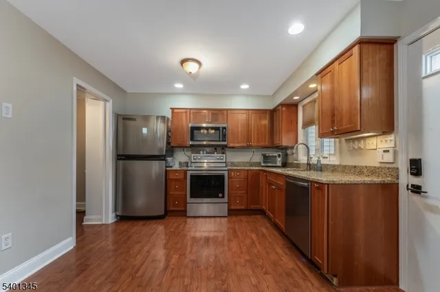 a kitchen with stainless steel appliances granite countertop a refrigerator a stove top oven a sink and dishwasher with wooden floor