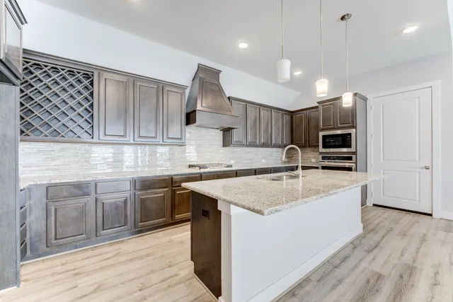 a kitchen with stainless steel appliances granite countertop a sink dishwasher a stove and a refrigerator with wooden floor