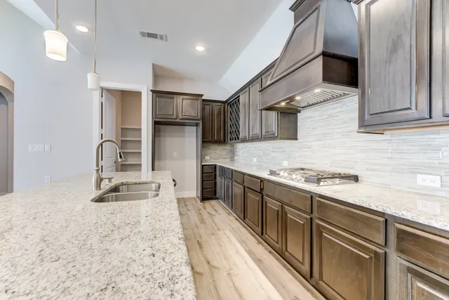 a kitchen with kitchen island granite countertop a stove top oven a sink a dining table and chairs with wooden floor