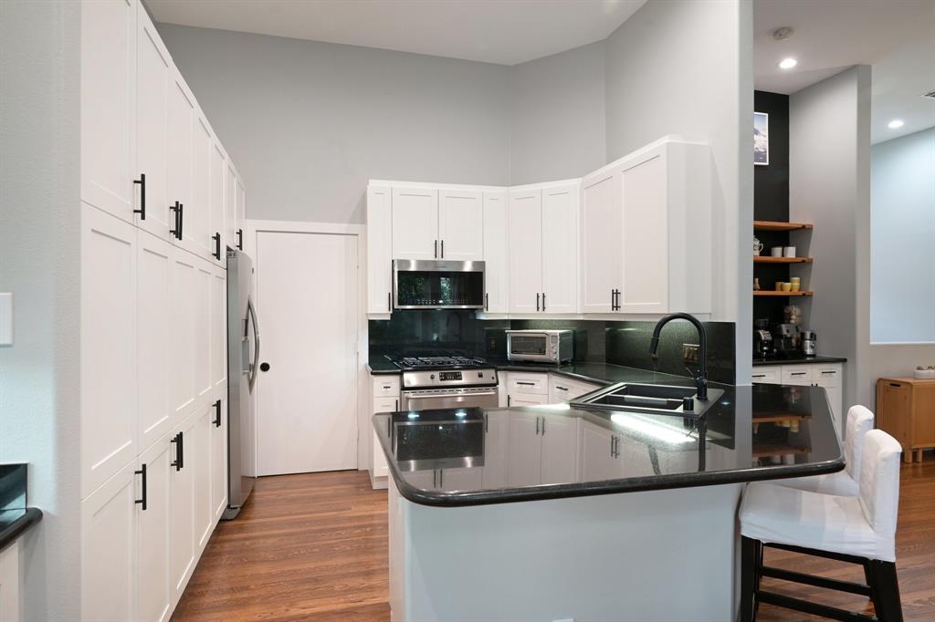 3553 Wheeler Street Dallas, TX 75209 - Photo 14 of 35 Kitchen featuring full-height white pantry cabinets, gas range, stainless steel appliances, and black granite backsplash