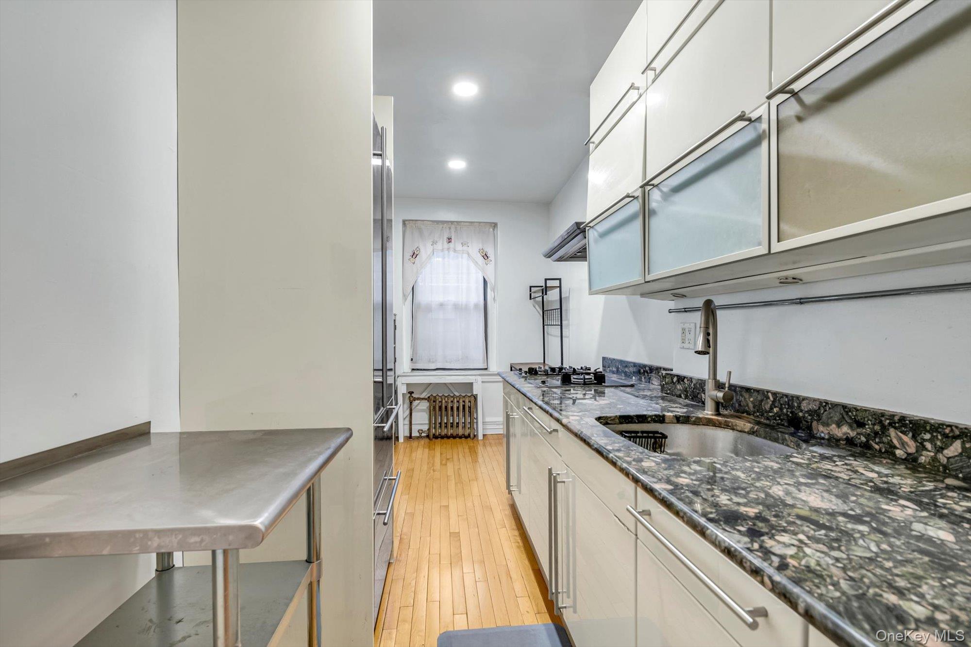 72-34 Austin Street, Unit F10 Queens, NY 11375 - Photo 8 of 15 Kitchen featuring dark stone countertops, light wood-style flooring, appliances with stainless steel finishes, recessed lighting, and exhaust hood