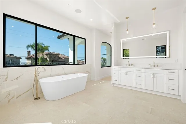 a bathroom with a double vanity sink a large mirror a bathtub and next to a window