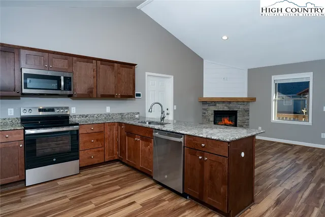 a kitchen with granite countertop a stove top oven a sink dishwasher and a microwave oven with wooden floor