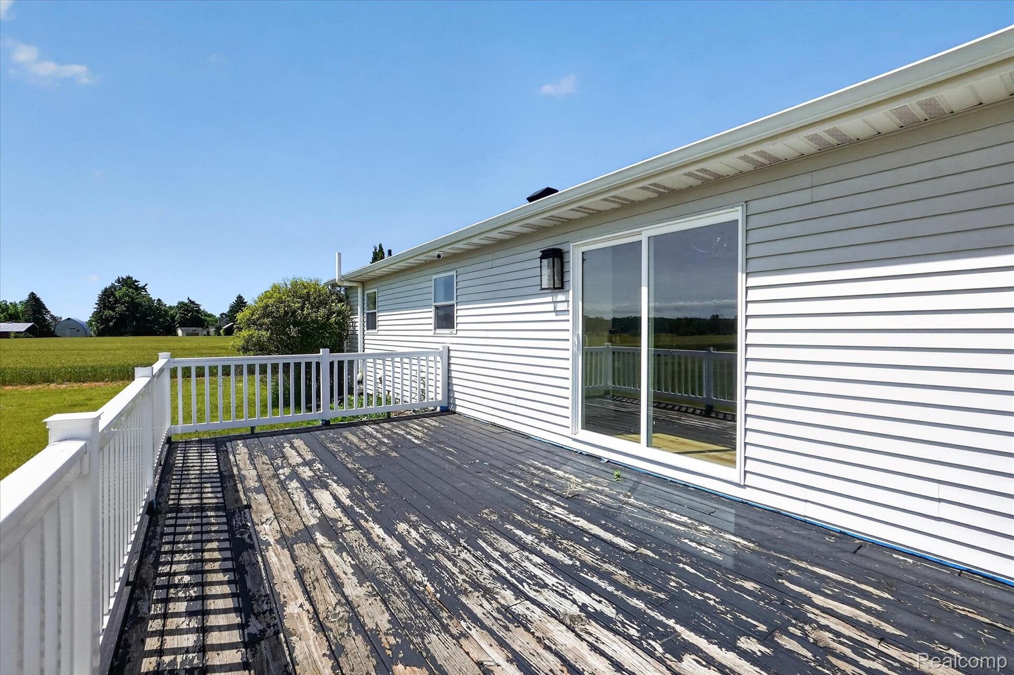 1400 North Every Road Mason, MI 48854 - Photo 27 of 33 Expansive rear deck with white railings, a sliding glass door, and an exterior wall light fixture