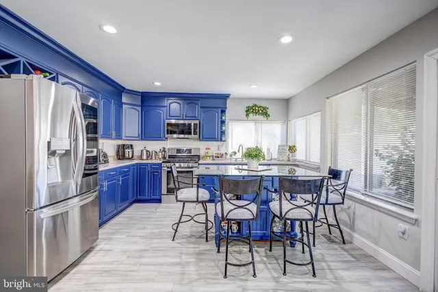 a kitchen with stainless steel appliances kitchen island granite countertop a refrigerator a stove a sink a dining table and chairs with wooden floor