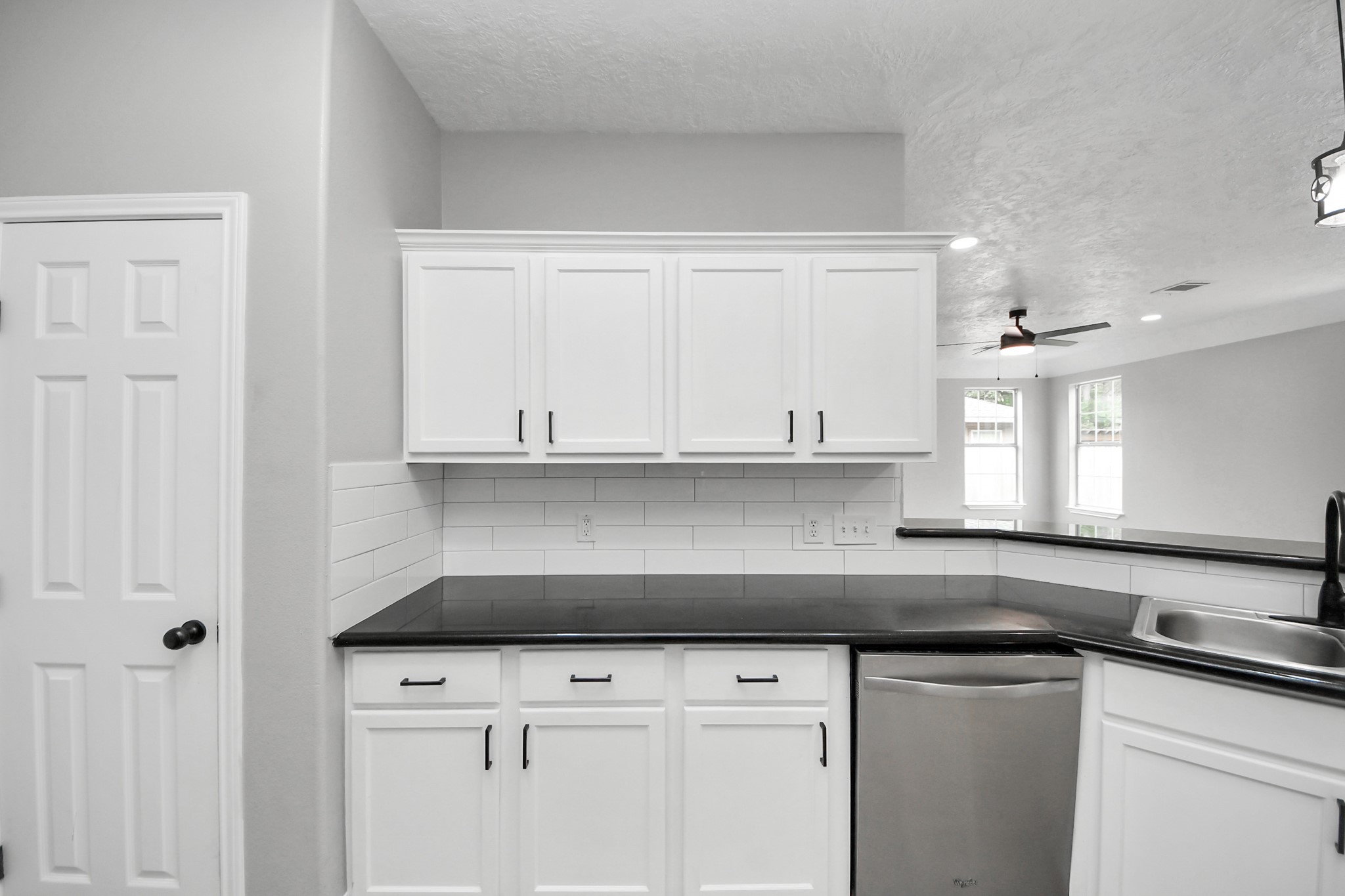 1105 East Kyle Road Clute, TX 77531 - Photo 13 of 44 This kitchen features modern white cabinetry with sleek black handles, a contrasting black countertop, and a stainless steel dishwasher. The open layout includes a breakfast bar and connects to a bright living area with large windows and recessed lighting.