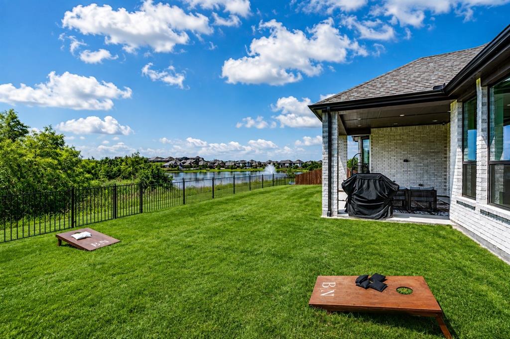 2150 Charming Frg Road Forney, TX 75126 - Photo 34 of 40 Expansive backyard with a manicured lawn, lake scenery, and wrought iron fencing