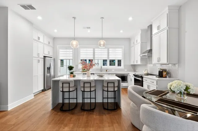 a kitchen with stainless steel appliances granite countertop a stove a sink dishwasher a refrigerator and white cabinets with wooden floor