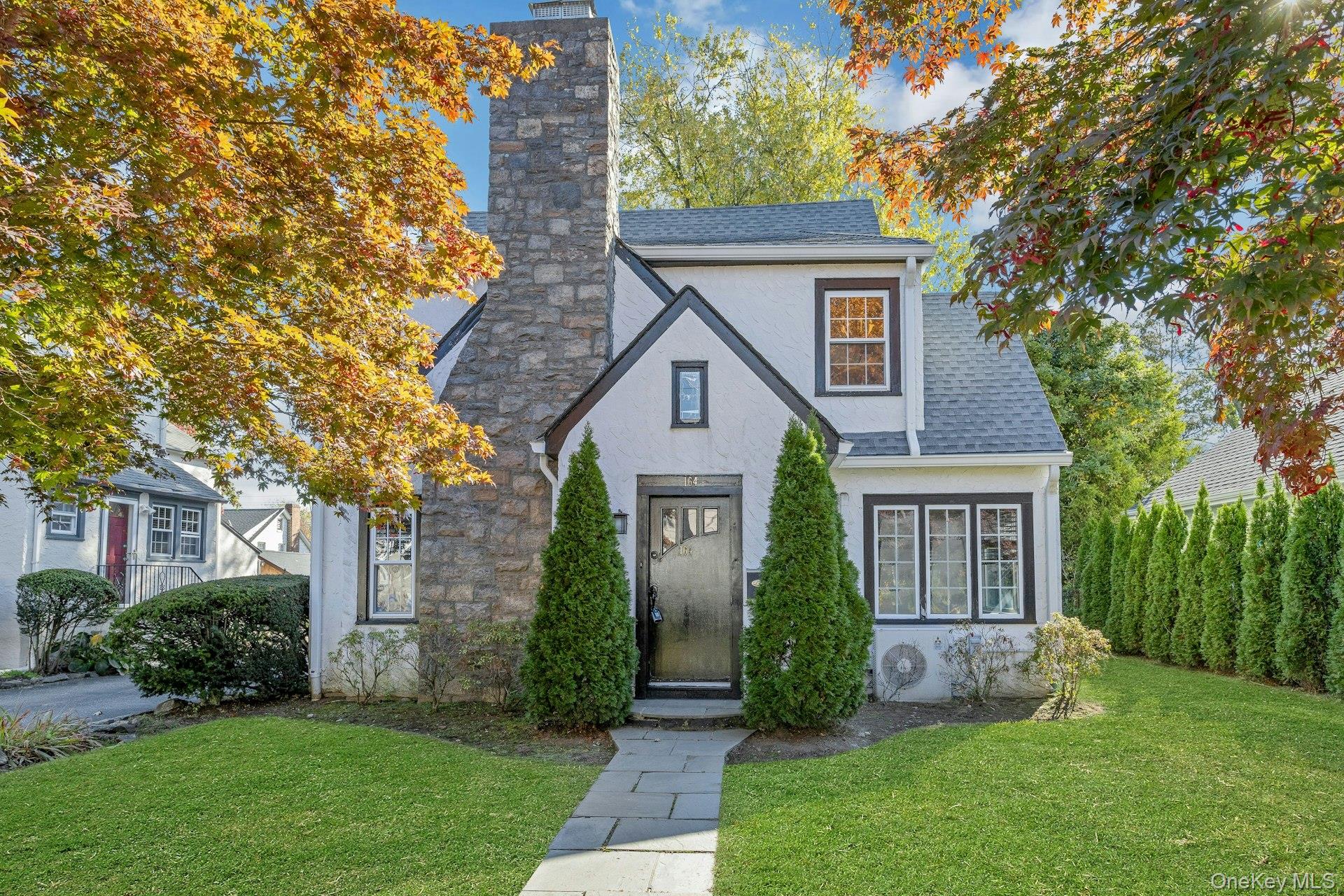 Tudor house featuring a chimney, stucco siding, and shingled roof.