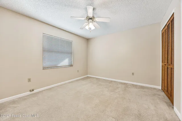 an empty room with a chandelier fan and windows