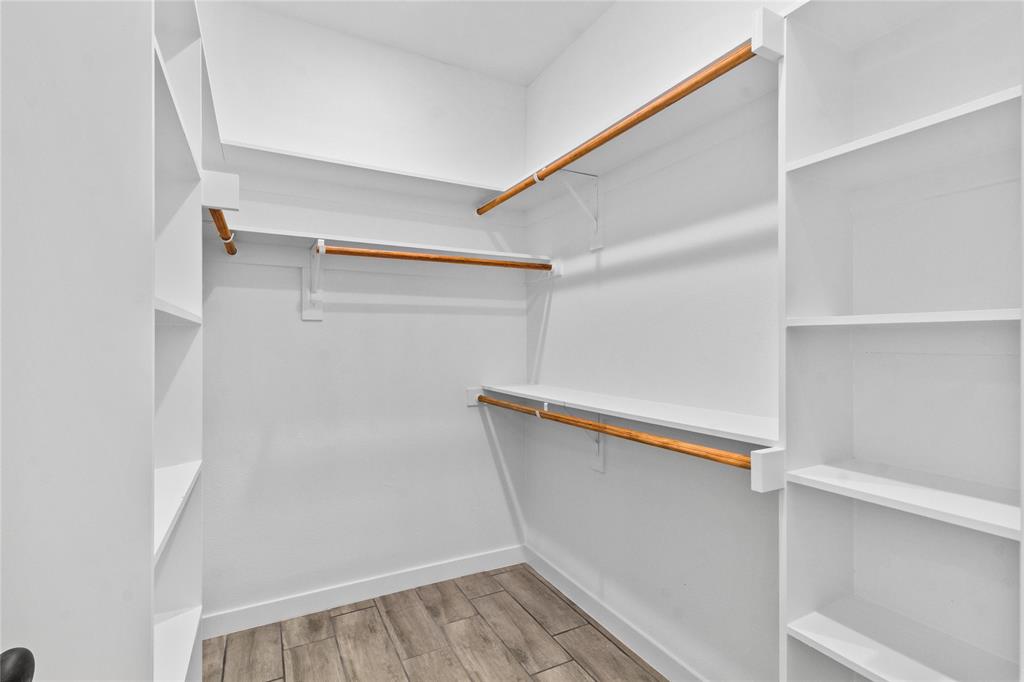 7520 Double Bridge Road Mabank, TX 75156 - Photo 19 of 32 Spacious walk-in closet featuring custom wood-finish hanging rods, white built-in shelving throughout, and wood-finish flooring