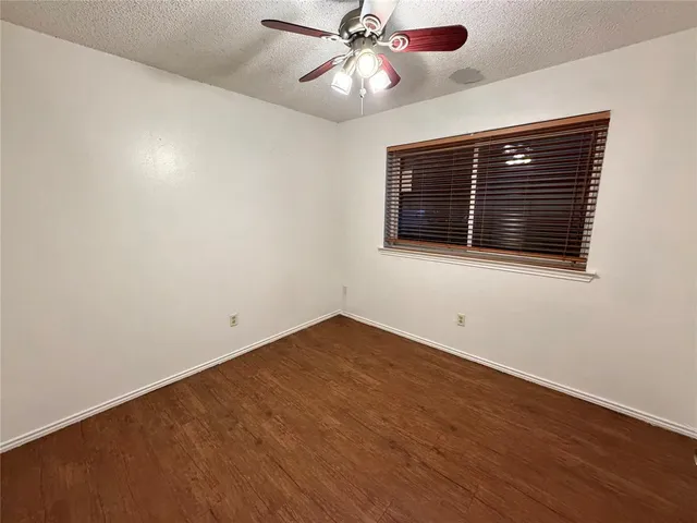 a view of an empty room with wooden floor and a ceiling fan