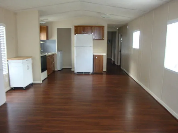 an empty room with wooden floor and a kitchen