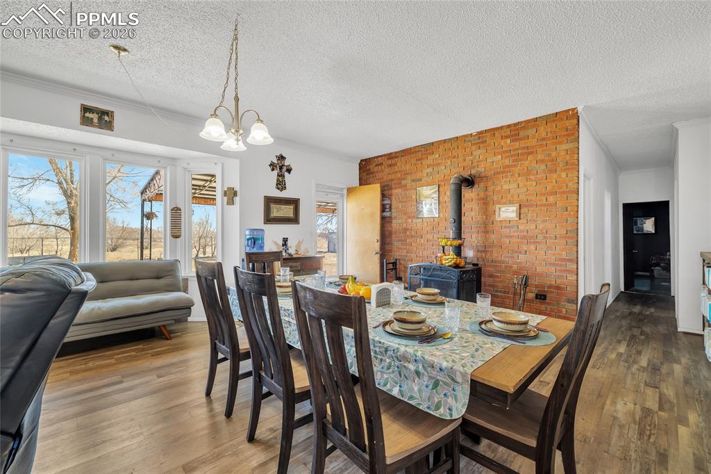 68300 Highway 50 Fowler, CO 81039 - Photo 21 of 47 Dining area featuring a wood stove, hardwood / wood-style floors, a textured ceiling, hanging lights, and brick wall