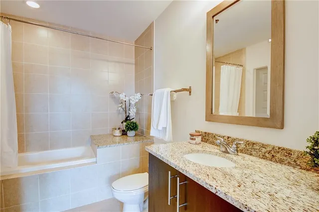 a bathroom with a granite countertop sink a toilet a mirror and shower