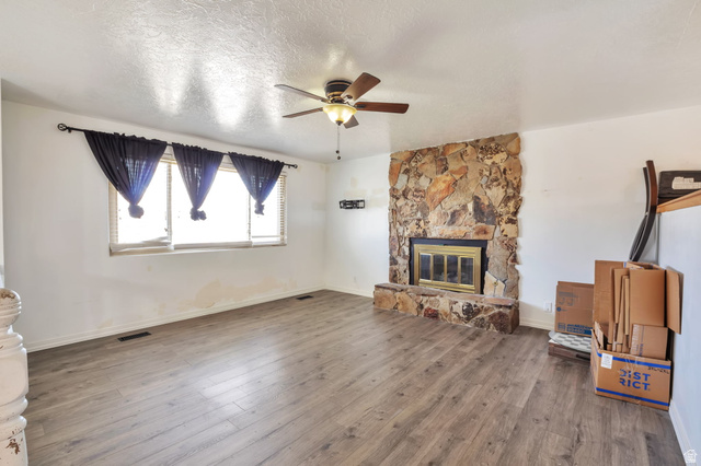 1057 North 700 West Clinton, UT 84015 - Photo 2 of 15 Unfurnished living room with ceiling fan, a textured ceiling, dark wood finished floors, and a stone fireplace