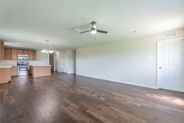 an empty room with wooden floor kitchen ceiling fan and kitchen view