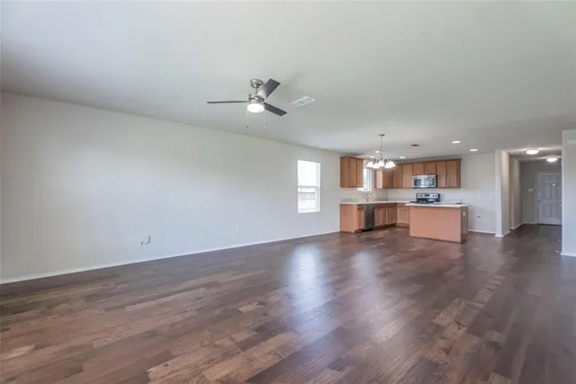 a view of an empty room with wooden floor and kitchen view