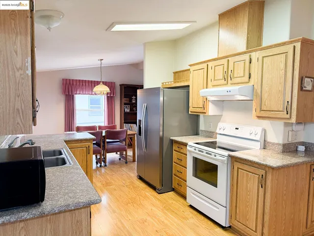 a kitchen with stainless steel appliances granite countertop a refrigerator a stove a sink dishwasher and white cabinets with wooden floor