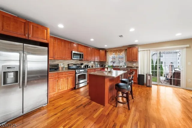 a kitchen with stainless steel appliances granite countertop a refrigerator a stove top oven a dining table and chairs with wooden floor