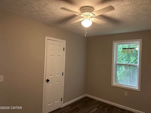 an empty room with wooden floor fan and windows