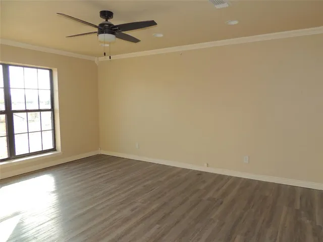 an empty room with wooden floor fan and windows