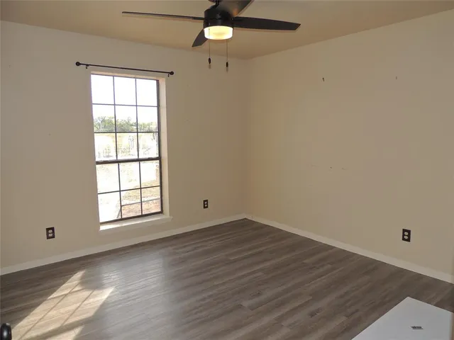 an empty room with wooden floor chandelier fan and windows