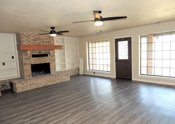 an empty room with wooden floor fireplace and windows