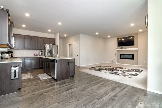 a kitchen with stainless steel appliances kitchen island granite countertop a stove top oven a sink dishwasher and white cabinets with wooden floor