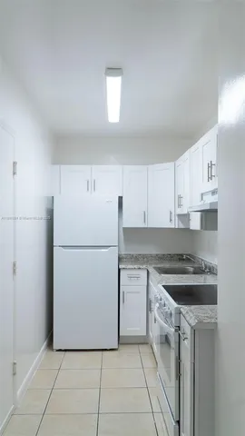 a kitchen with a sink a refrigerator and white cabinets