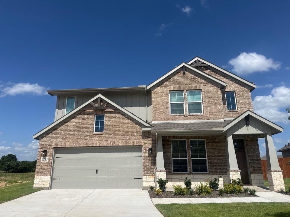 1233 Frio Drive Springtown, TX 76082 - Photo 1 of 13 Two-story residence featuring a brick and stone facade with vertical siding accents, an attached two-car garage, covered entry porch, and mature landscaping