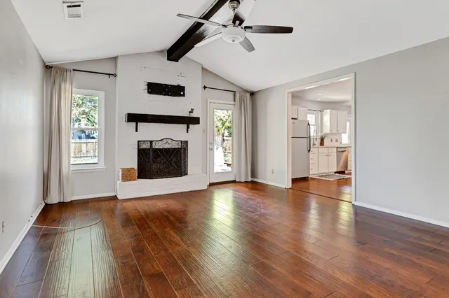 a view of an empty room with wooden floor fireplace and a window