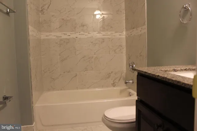 a bathroom with a granite countertop bathtub shower sink vanity and toilet