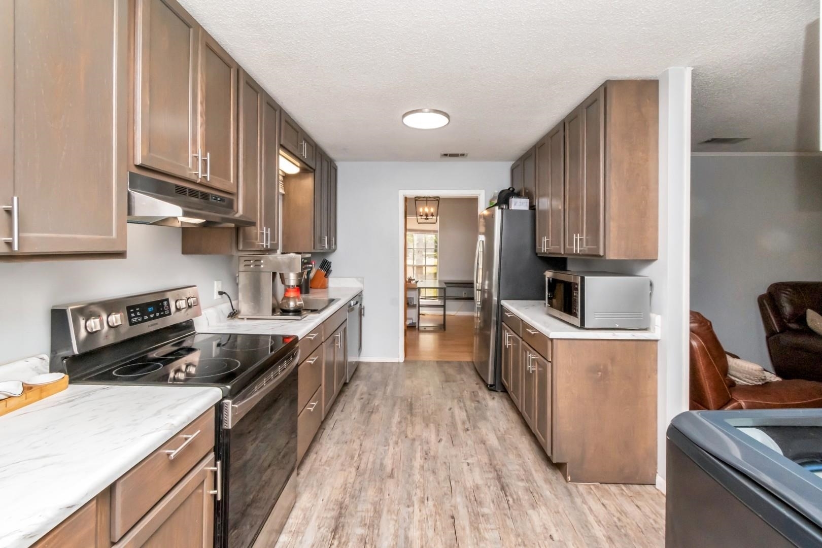 6405 1st Street Wilmer, AL 36587 - Photo 11 of 38 Kitchen featuring stainless steel appliances, a textured ceiling, light countertops, light wood-style flooring, and under cabinet range hood