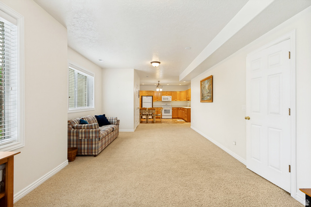 298 North Canyon Road Bountiful, UT 84010 - Photo 35 of 57 Carpeted living area with two windows, featuring a kitchen beyond with wood cabinetry and white appliances