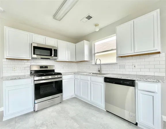 a kitchen with granite countertop white cabinets sink and stainless steel appliances