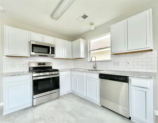 a kitchen with granite countertop white cabinets sink and stainless steel appliances
