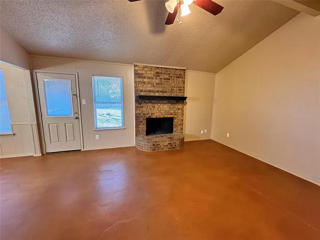 an empty room with ceiling fan fireplace and window